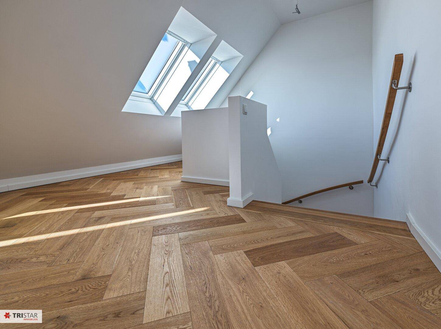 Heller Flur mit Holztreppe, Fischgrätparkett und Dachfenstern, die den Raum erhellen.