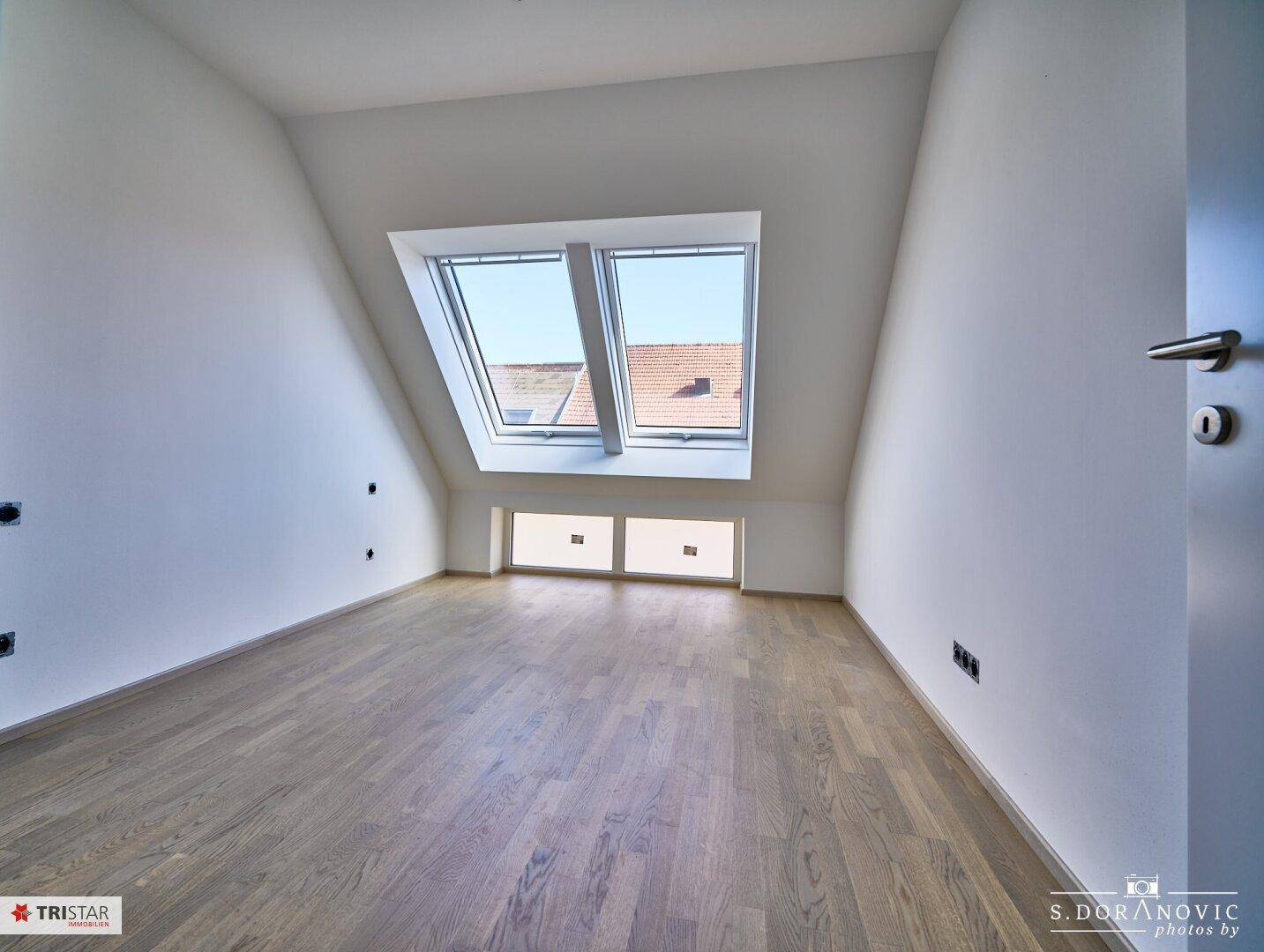 Helles Zimmer im Dachgeschoss mit Holzboden, schrägen Wänden und Dachfenstern.