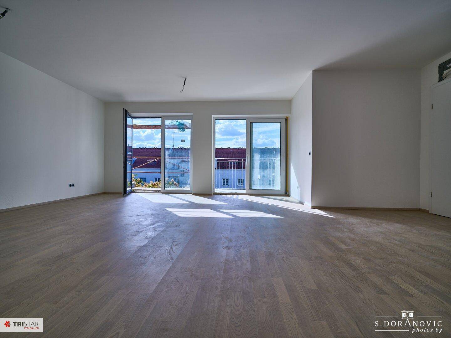 Geräumiger, heller Wohnbereich mit Parkettboden und viel Tageslicht durch große Fenster.