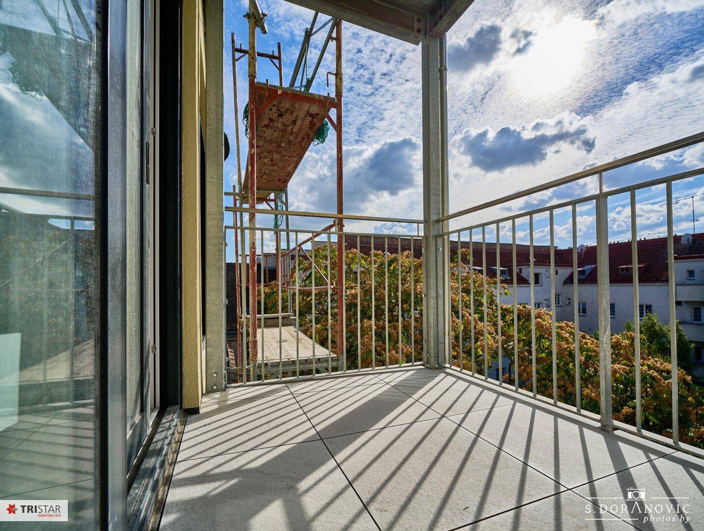 Balkon mit Fliesenboden und Metallgeländer, bietet einen Blick auf die Stadt und Baustelle.