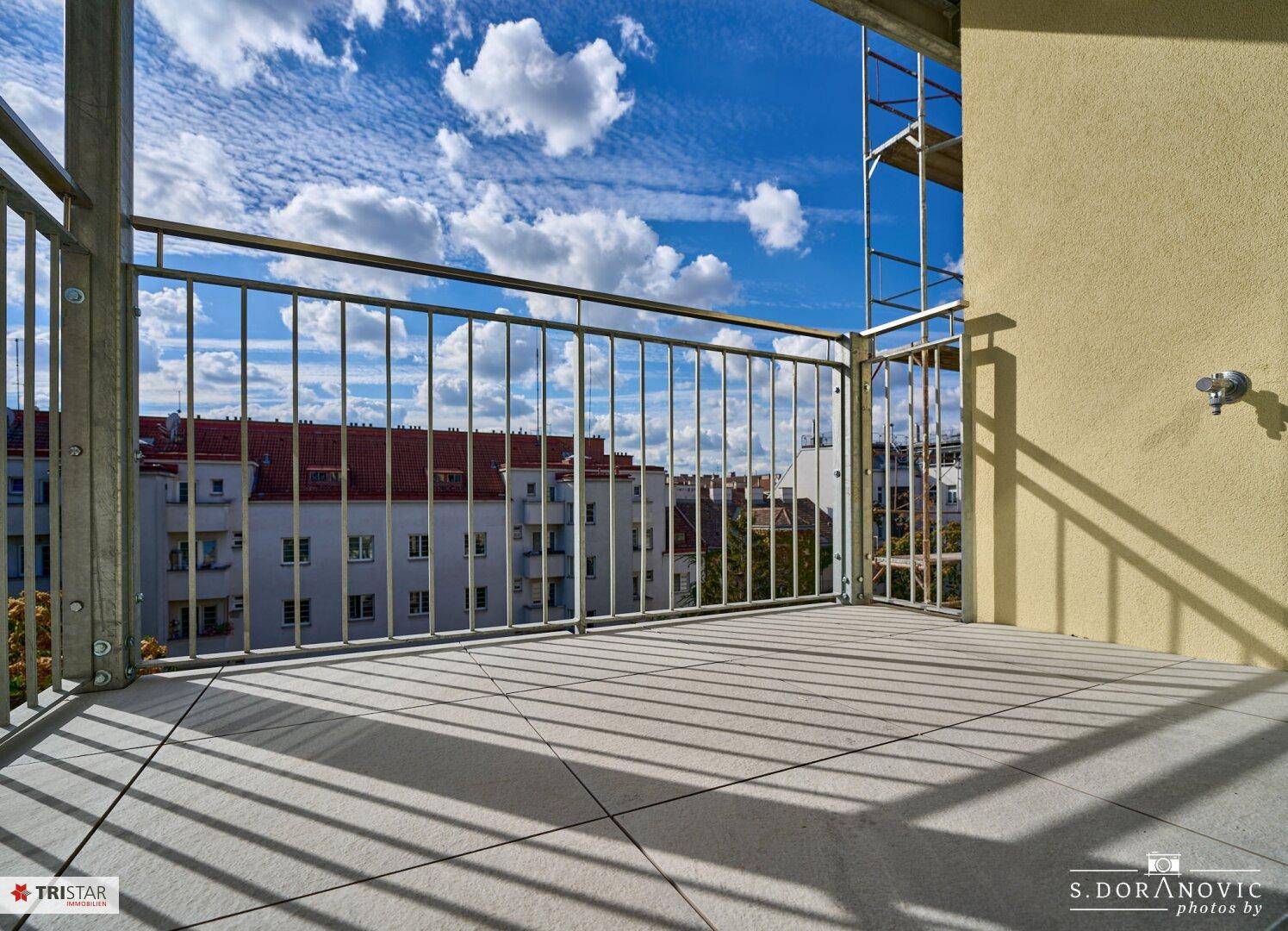 Sonniger Balkon mit Fliesenboden und Metallgeländer, bietet einen weiten Stadtblick.