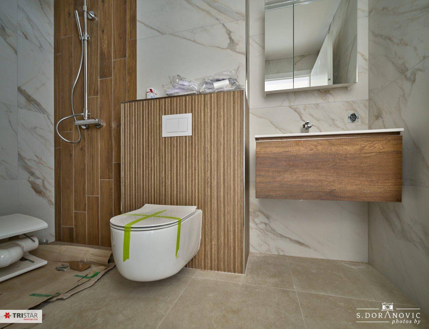 Detailansicht des modernen Badezimmers mit Wand-WC, Waschtisch und Marmoroptik-Fliesen.