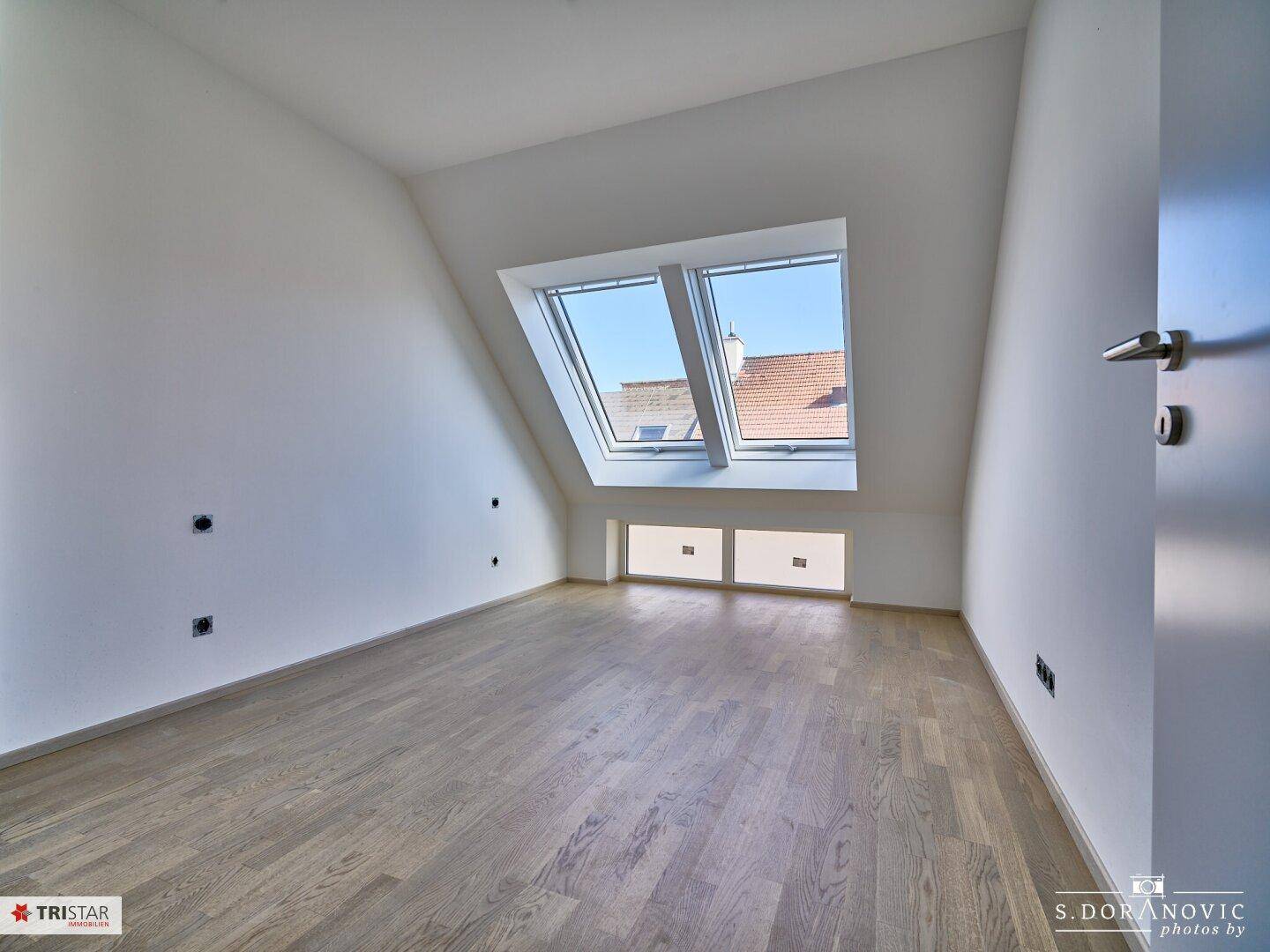 Geräumiges Dachzimmer mit Holzboden und großen Dachfenstern, die viel Licht spenden.