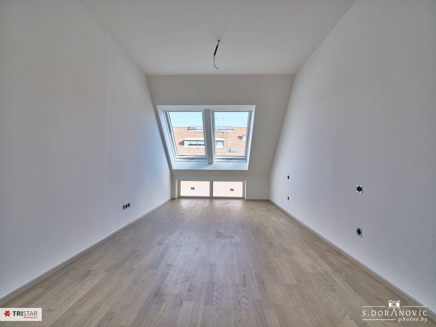 Geräumiges Dachzimmer mit schrägen Wänden, Holzboden und großen Dachfenstern.