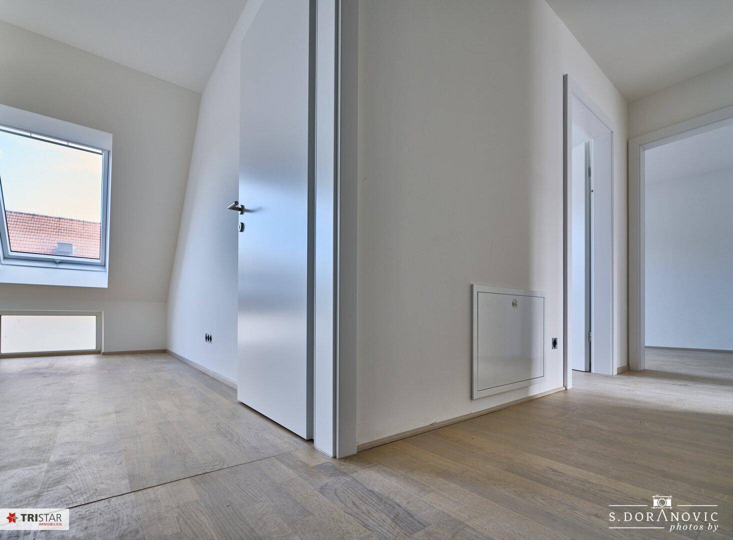 Heller Flur mit Holzboden und weißen Türen, der zu verschiedenen Zimmern führt.