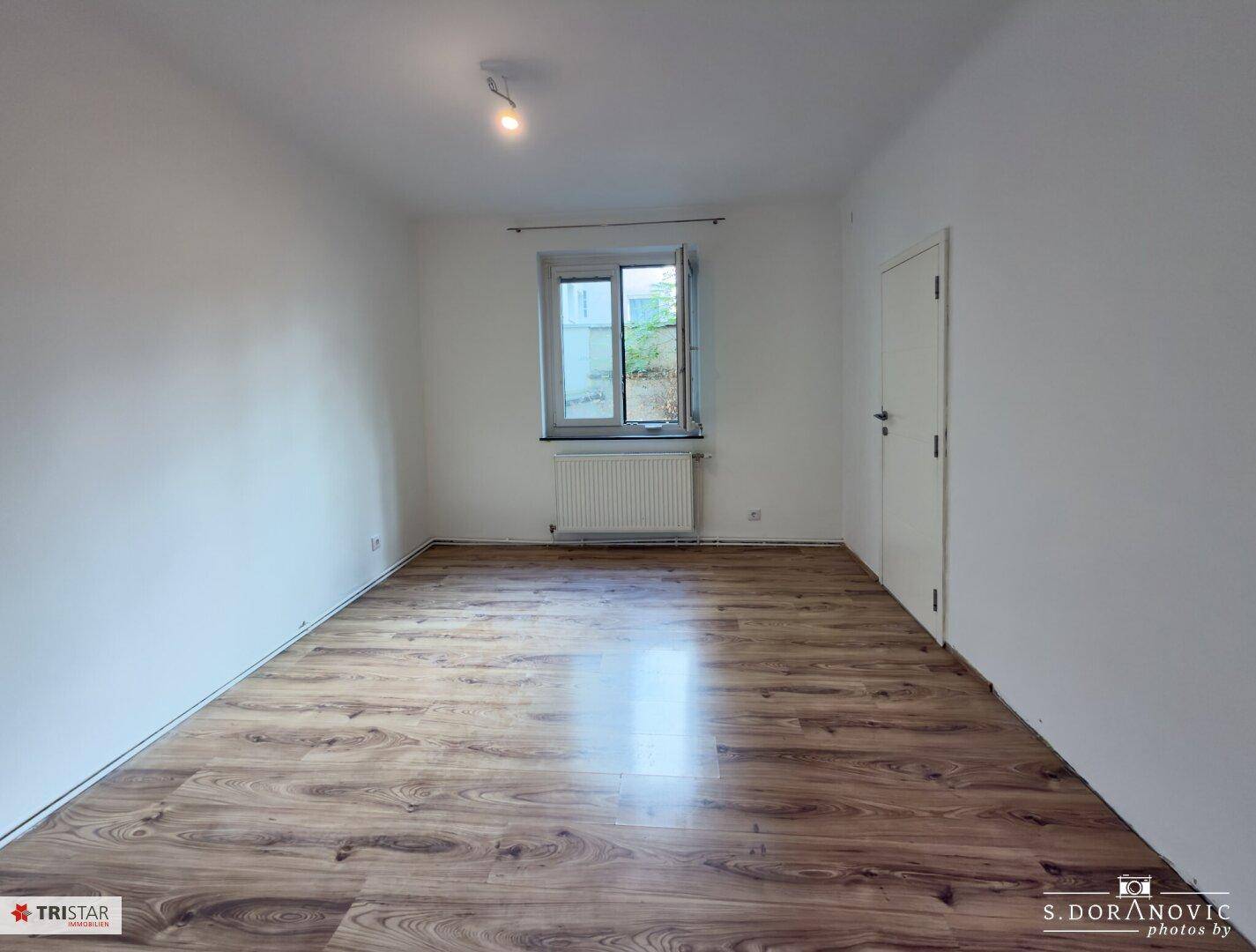 Helles Zimmer mit Laminatboden und Fenster, das eine angenehme Wohnatmosphäre schafft.