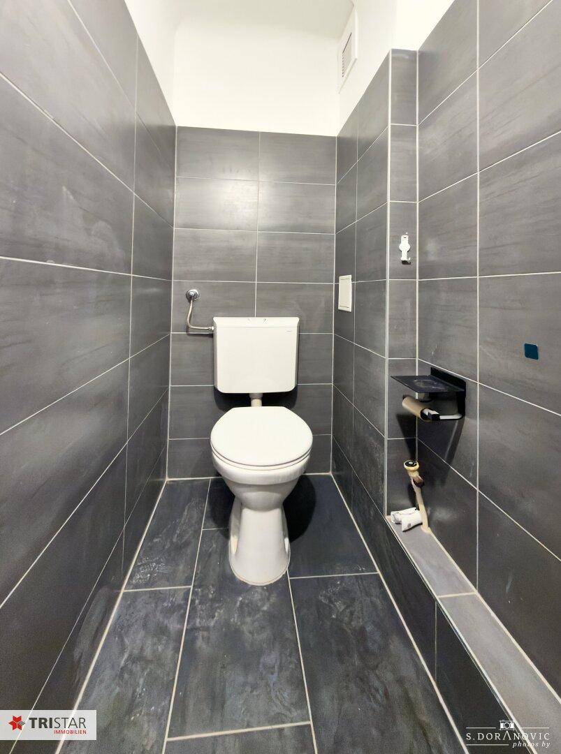 Separates WC mit modernen grauen Fliesen an Wänden und Boden, bietet Privatsphäre.