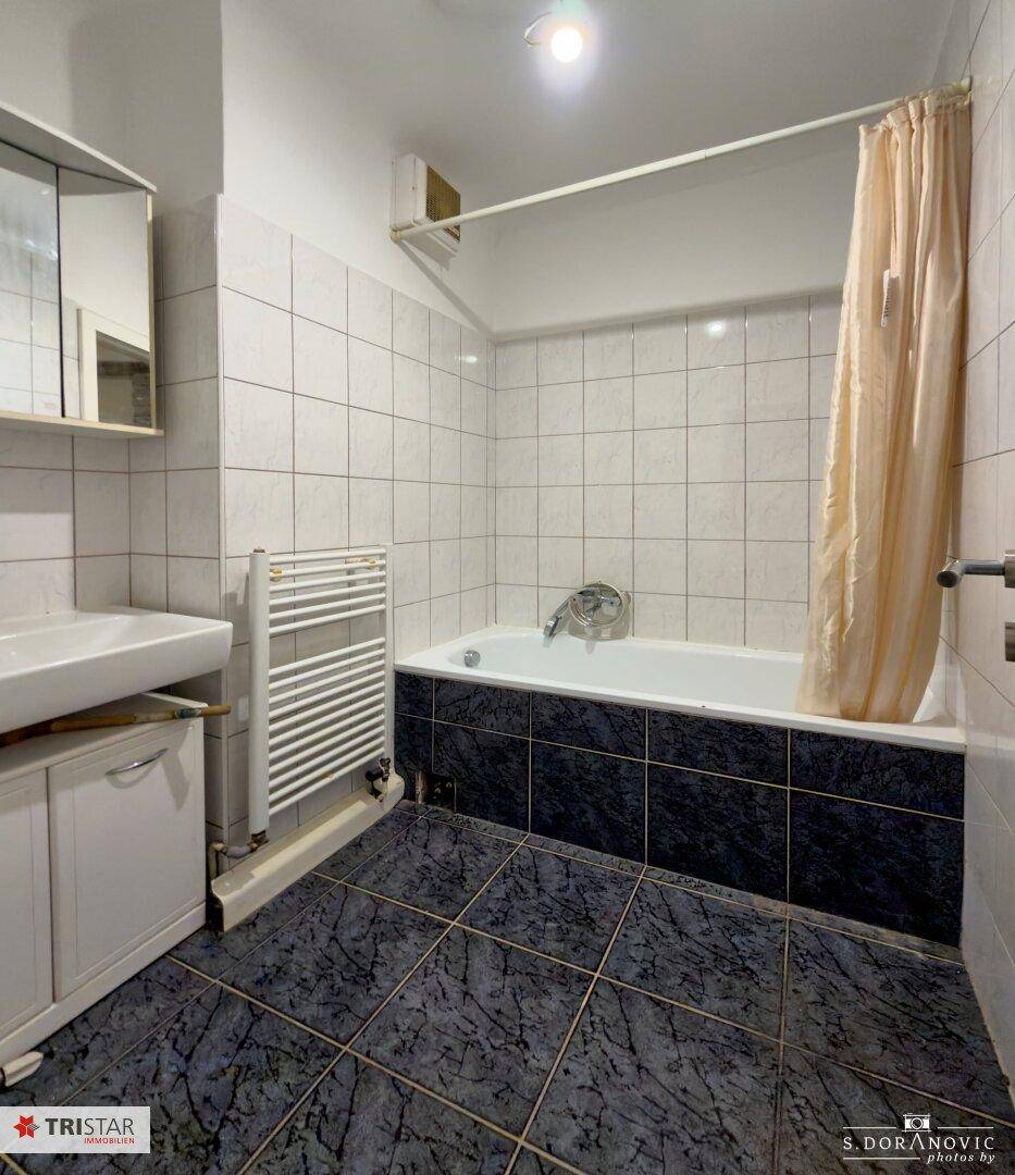 Badezimmer mit Badewanne, Waschbecken, Spiegelschrank und beheiztem Handtuchhalter, komplett gefliest.