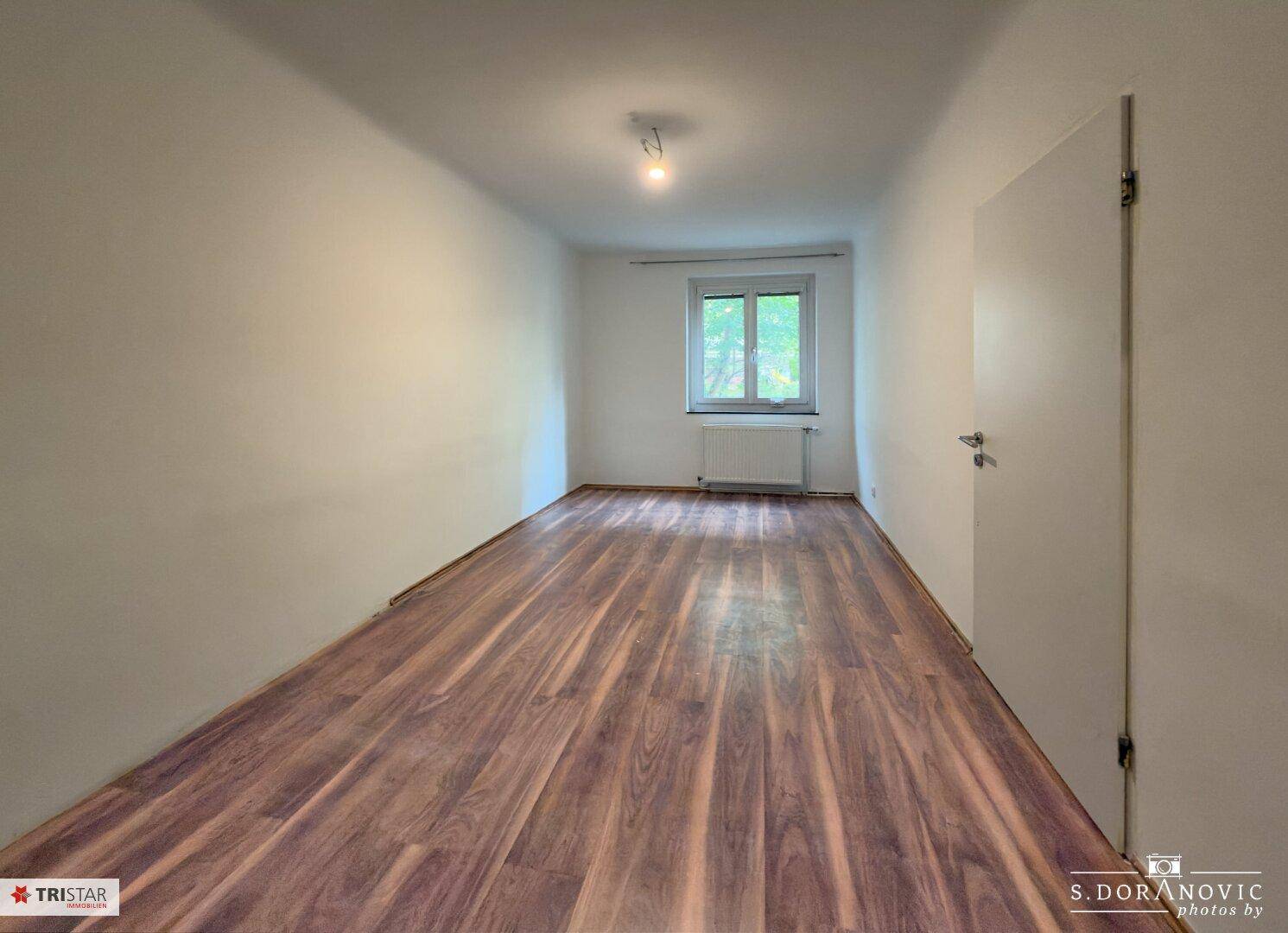 Gemütliches Zimmer mit Laminatboden und einem Fenster, das viel Tageslicht hereinlässt.