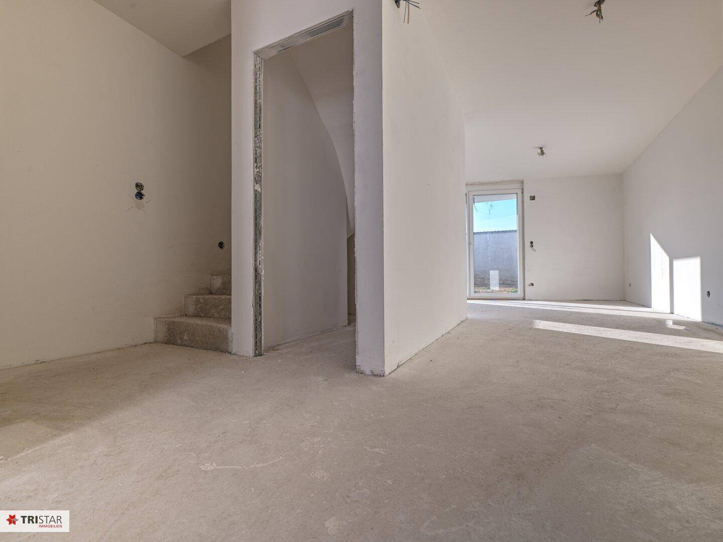 Unfertiger Eingangsbereich mit Treppenaufgang und viel Tageslicht, bereit für den Innenausbau.