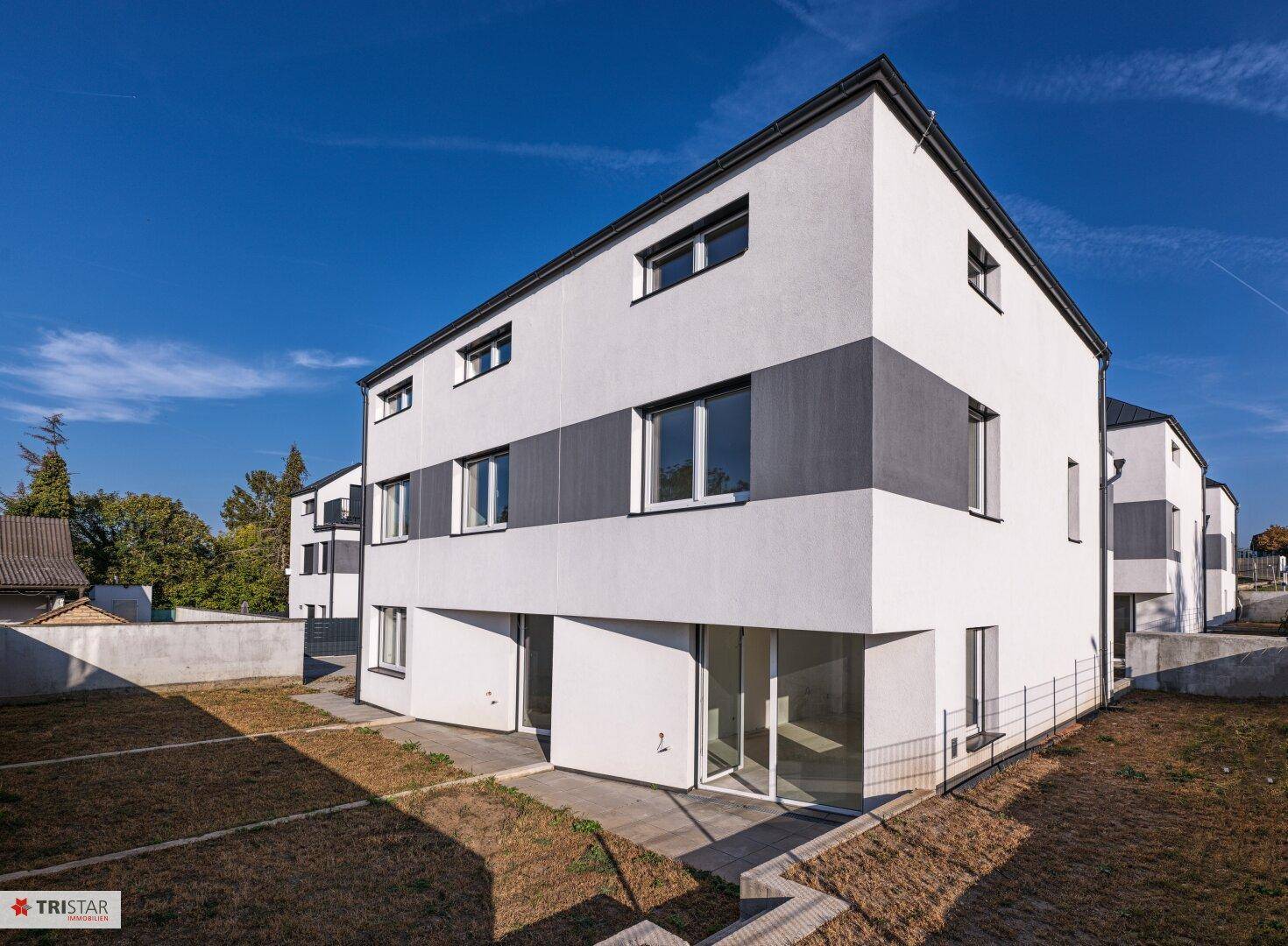 Ansicht eines modernen Reihenhauses mit heller Fassade und großen Fenstern unter blauem Himmel.