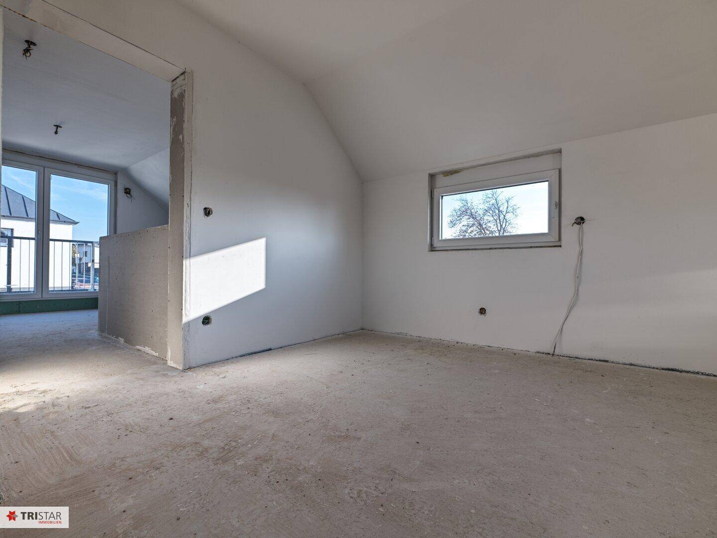 Unfertiger Raum im Dachgeschoss mit schräger Decke und Fenster, bereit für den Ausbau.
