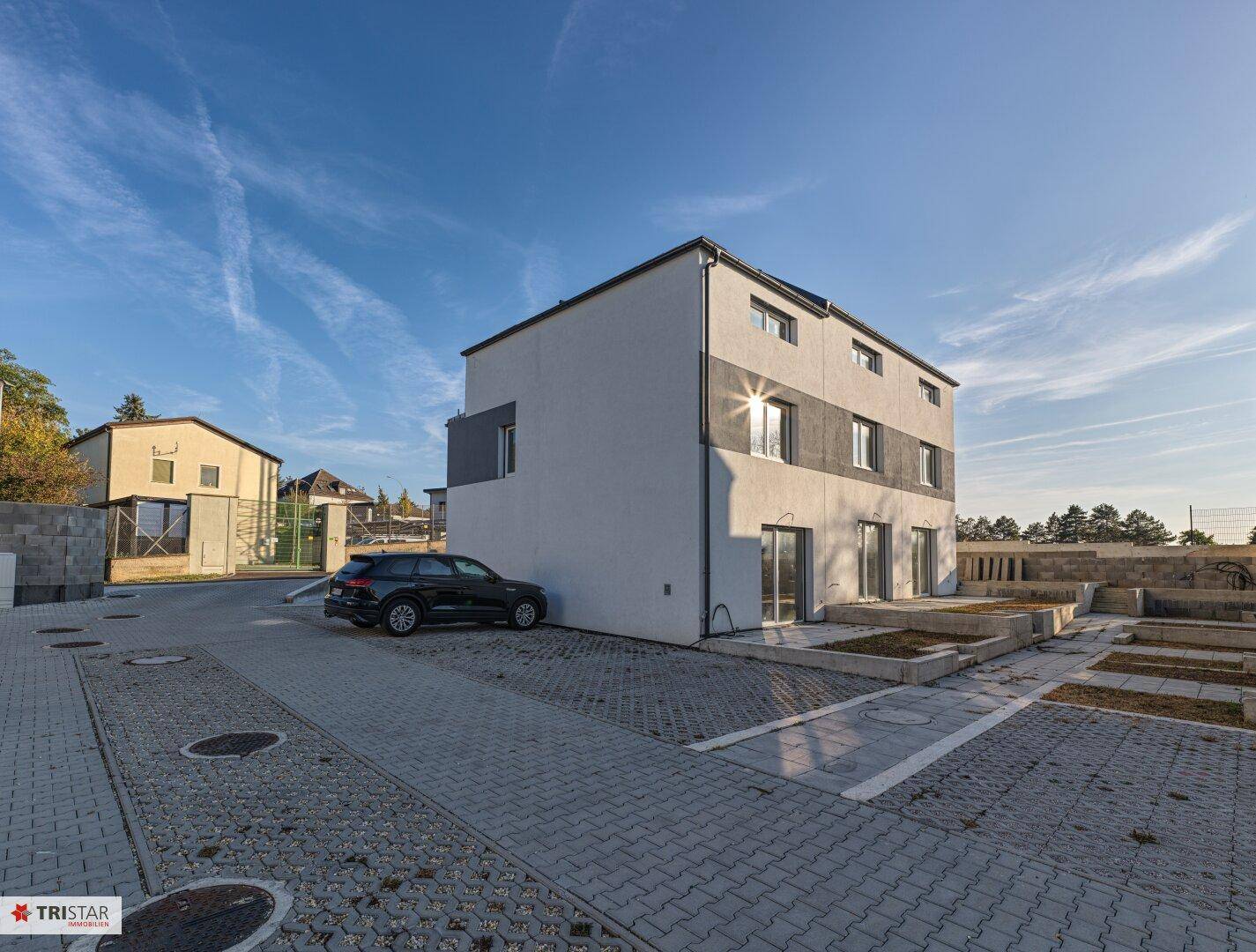 Neubau-Mehrfamilienhaus mit moderner Architektur und gepflasterten Parkplätzen im Außenbereich.