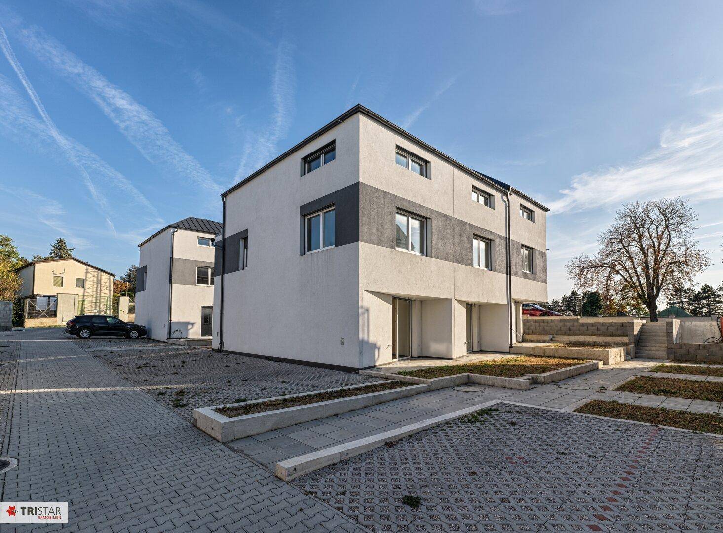 Neubau-Mehrfamilienhaus mit moderner Architektur und gepflasterten Parkplätzen im Außenbereich.