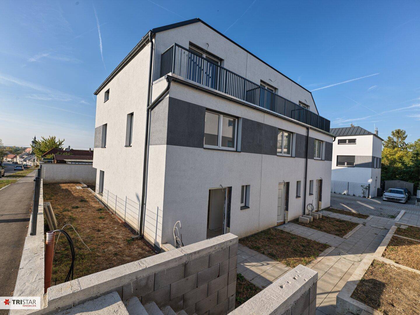 Modernes Reihenhaus mit Balkon im Obergeschoss und unfertigem Gartenbereich unter klarem Himmel.