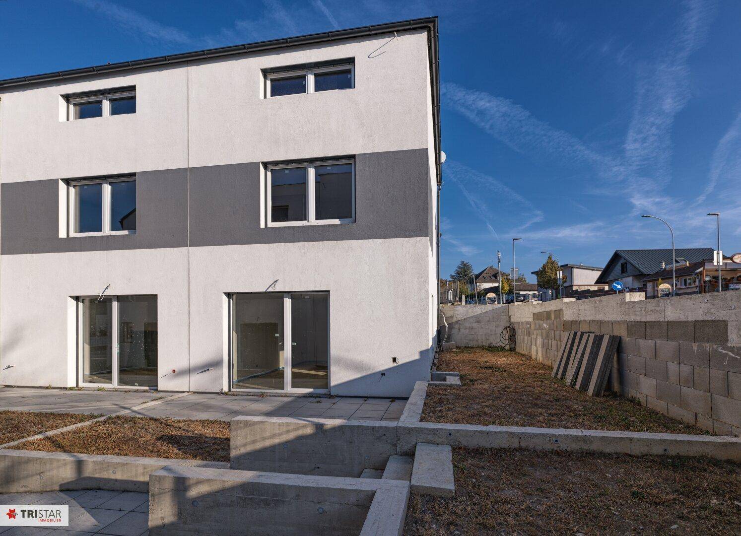 Rückseite eines modernen Reihenhauses mit Terrassenzugang und unfertigem Gartenbereich.