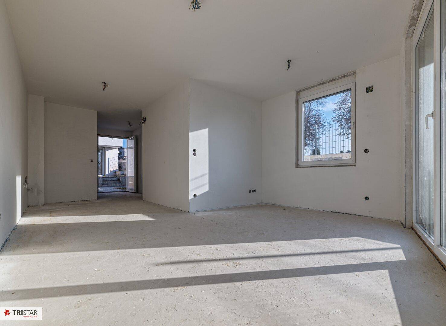 Geräumiger Wohnraum im Rohbauzustand mit viel Tageslicht und Blick ins Grüne.