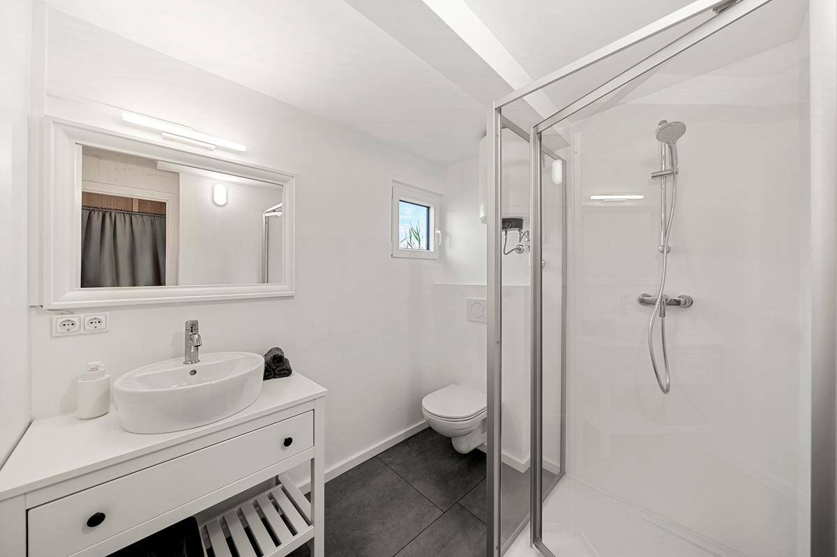 Modernes Badezimmer mit Dusche, WC, Waschtisch und einem kleinen Fenster für natürliche Belüftung.