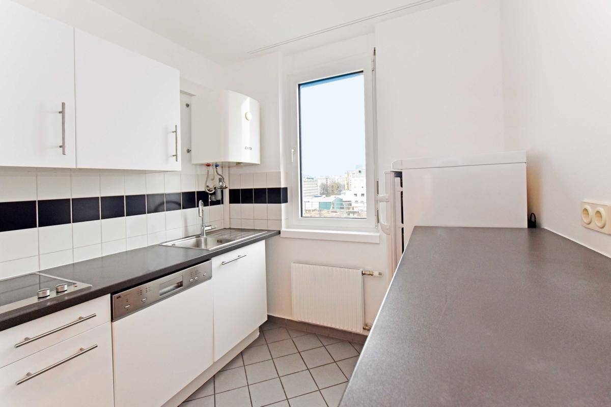 Funktionale Küche mit weißen Schränken, dunkler Arbeitsplatte und Fenster, ausgestattet mit Spülmaschine.