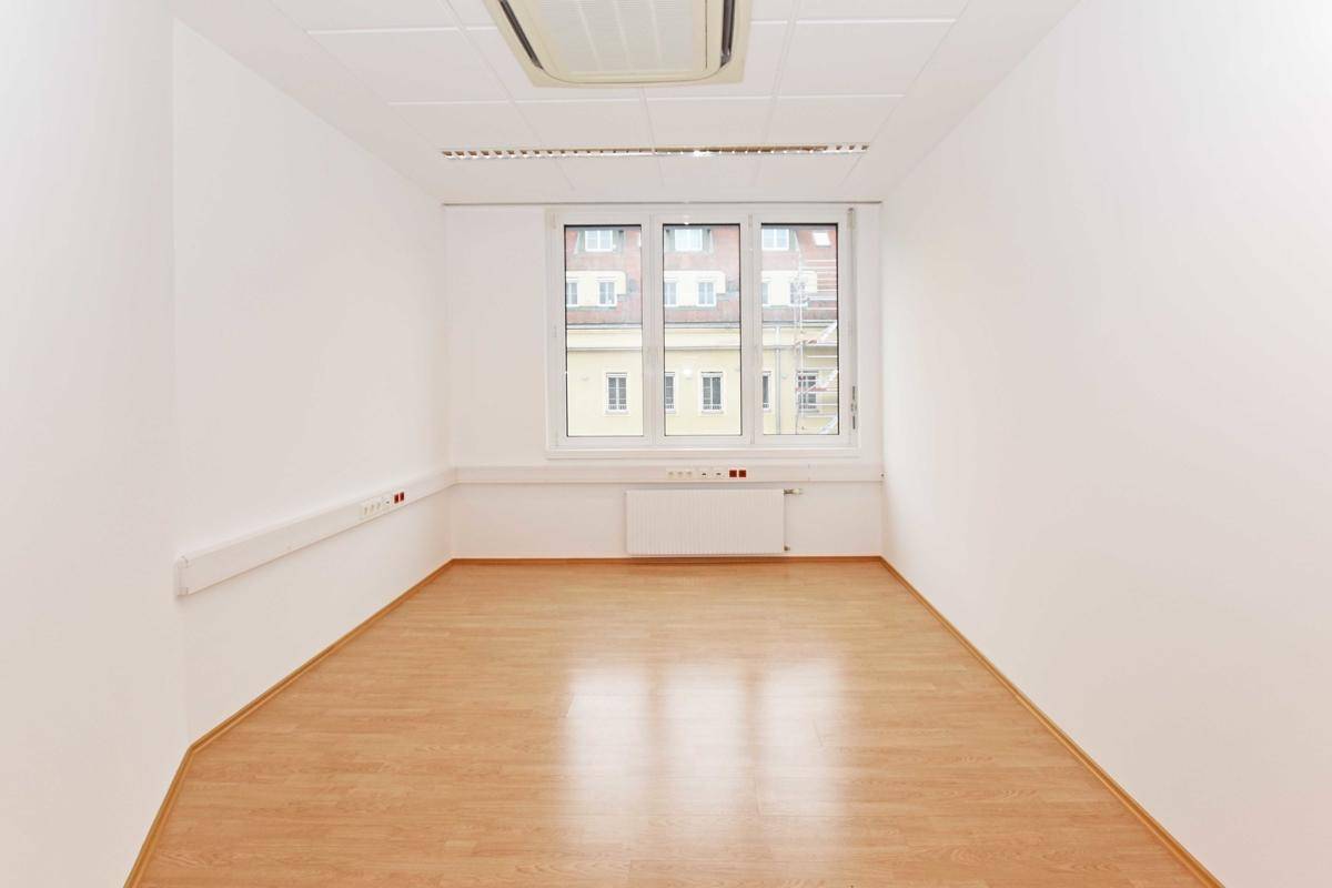 Kompaktes Büro mit Laminatboden, Klimaanlage und einem großen Fenster, das viel Tageslicht hereinlässt.