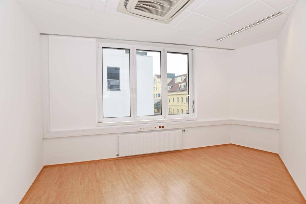 Helles Büro mit Laminatboden, Klimaanlage und einem Fenster mit Blick auf die Stadt, ideal für Einzelbüros.