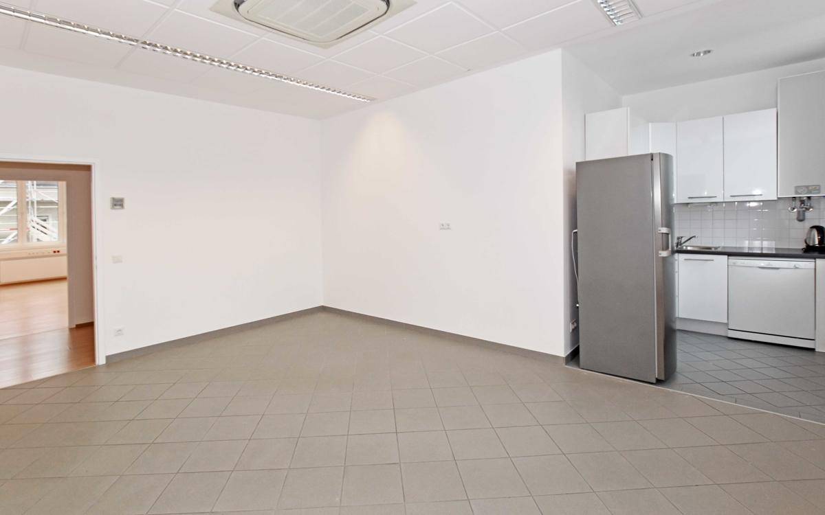 Funktionale Küchenzeile mit weißen Schränken, Spülmaschine und Kühlschrank, angrenzend an einen gefliesten Bereich.