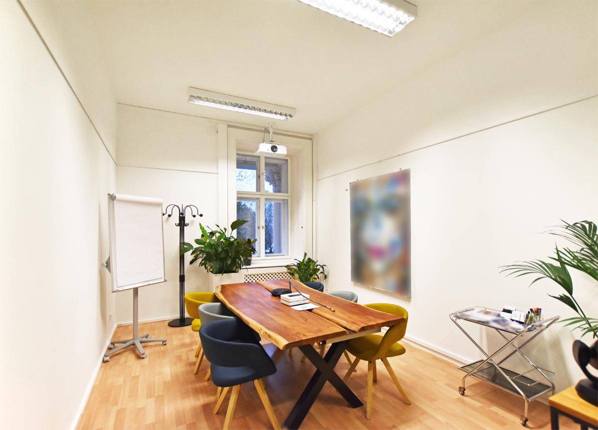 Heller Konferenzraum mit rustikalem Holztisch, modernen Stühlen und einem Fenster mit Grünblick.