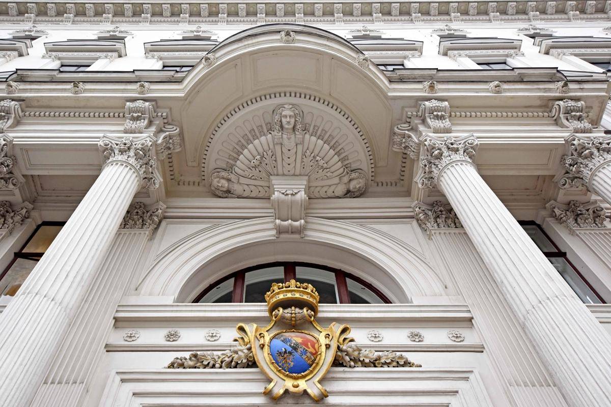 Detailaufnahme der reich verzierten Fassade eines historischen Gebäudes mit Säulen und einem Wappen.