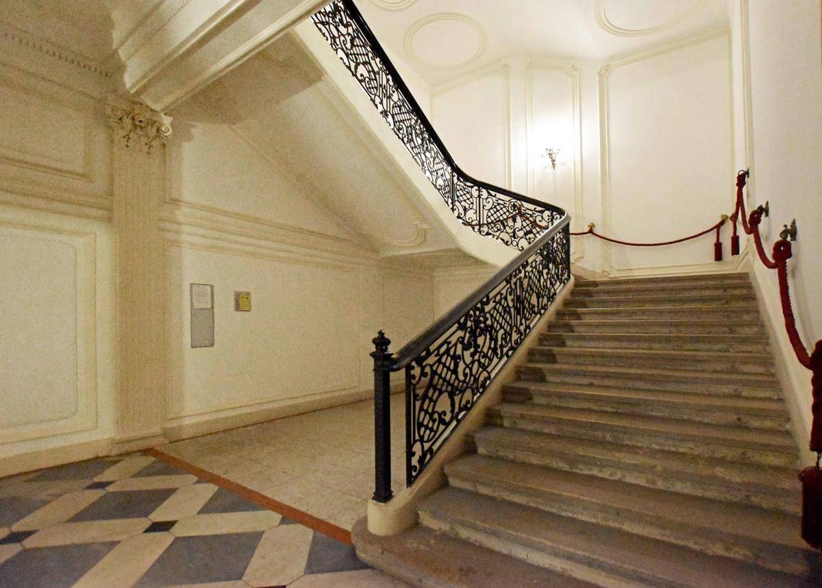 Elegantes Treppenhaus mit geschwungener Steintreppe, schmiedeeisernem Geländer und hohen Wänden mit Stuck.