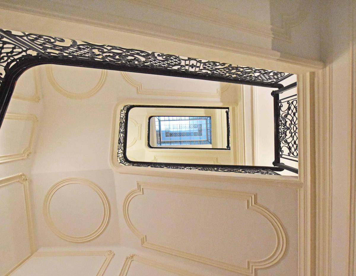 Blick von oben in ein historisches Treppenhaus mit kunstvollem Geländer und Stuckverzierungen an den Wänden.