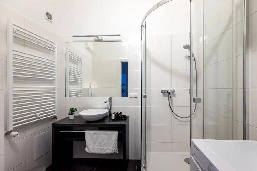 Modernes Badezimmer mit Duschkabine, stilvollem Waschbecken und Handtuchheizkörper in weißer Fliesenoptik.