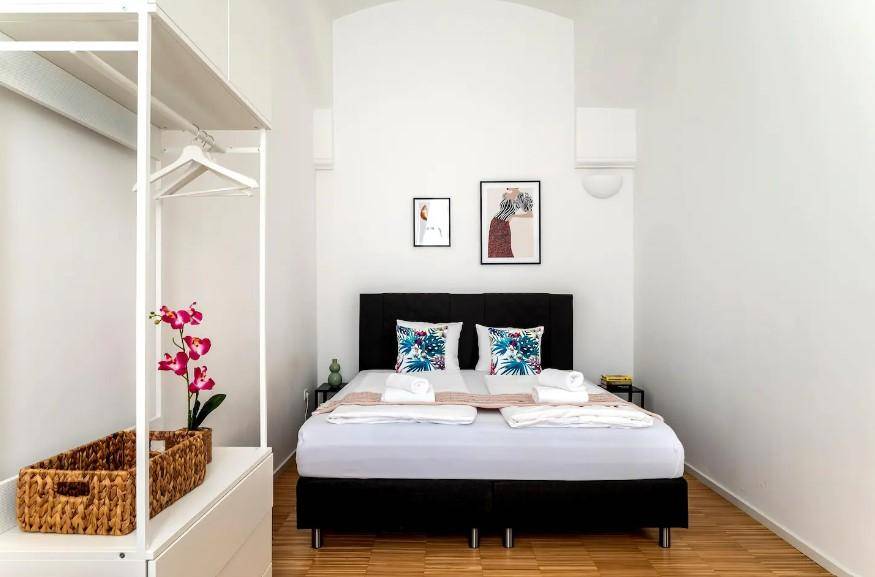 Modernes Schlafzimmer mit Doppelbett, offenem Kleiderschrank und minimalistischer Dekoration für eine ruhige Atmosphäre.