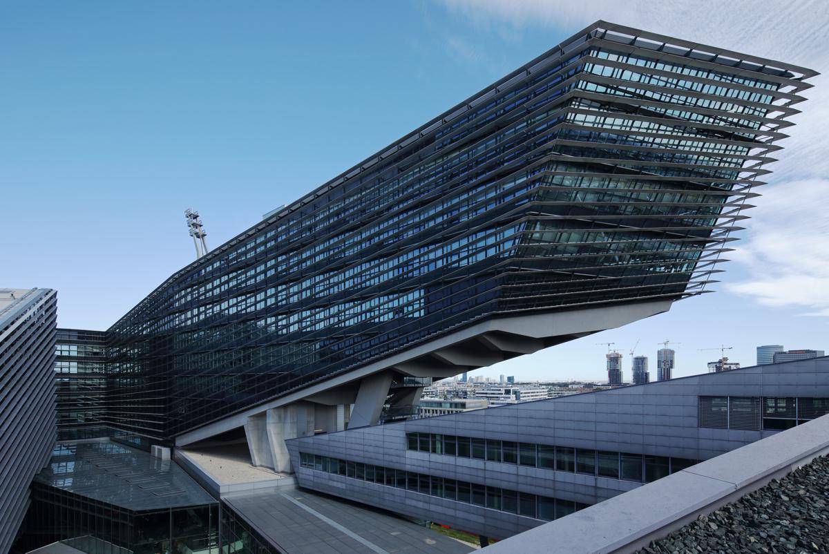 Beeindruckendes modernes Gebäude mit auskragender Architektur und großer Glasfassade unter blauem Himmel.