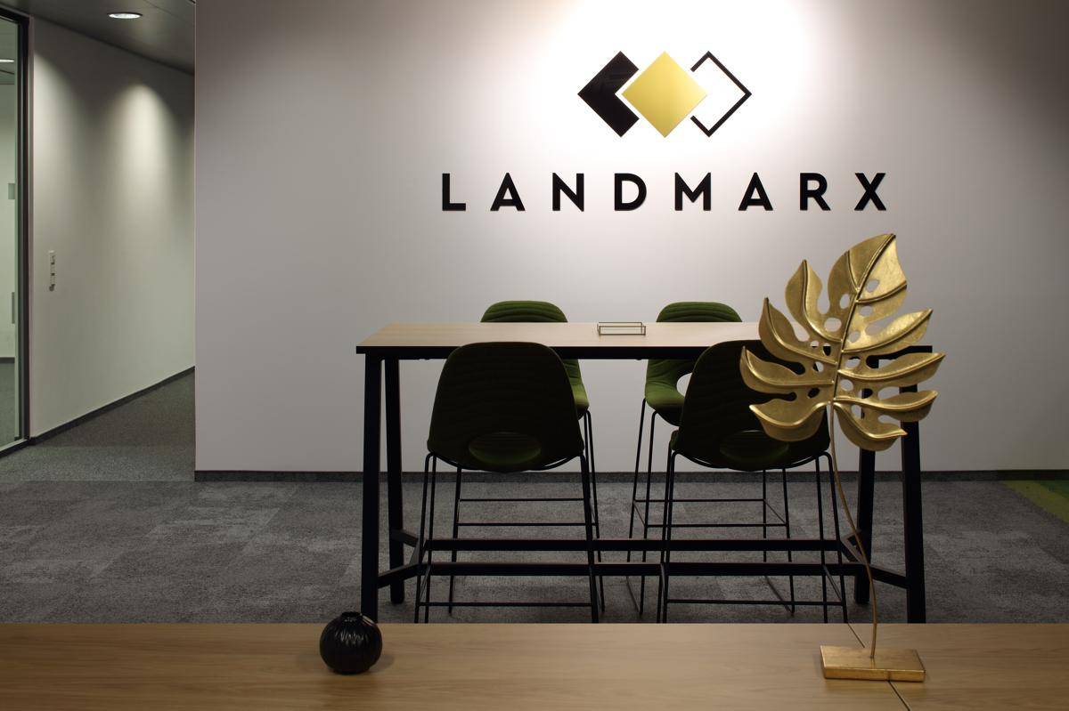 Detailansicht des Empfangsbereichs mit Firmenlogo, Stehtisch und dekorativem goldenen Blatt auf einer Holzoberfläche.