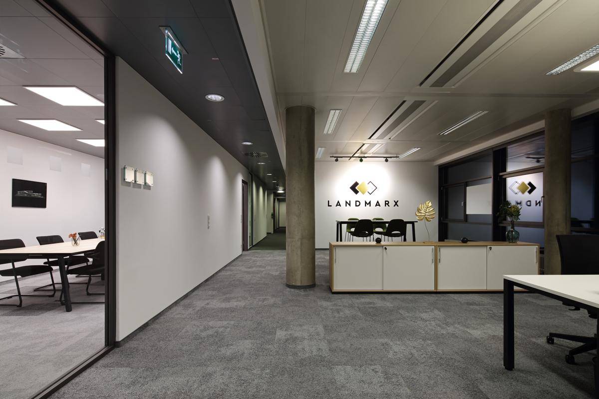 Moderner Bürobereich mit Teppichboden, langen Fluren und einem Empfangsbereich mit Firmenlogo an der Wand.