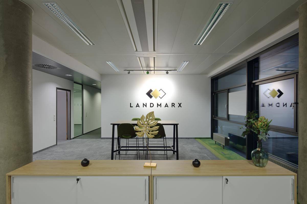 Geräumiger Empfangsbereich in einem modernen Büro mit Firmenlogo, Stehtisch und Blick auf die Fensterfront.