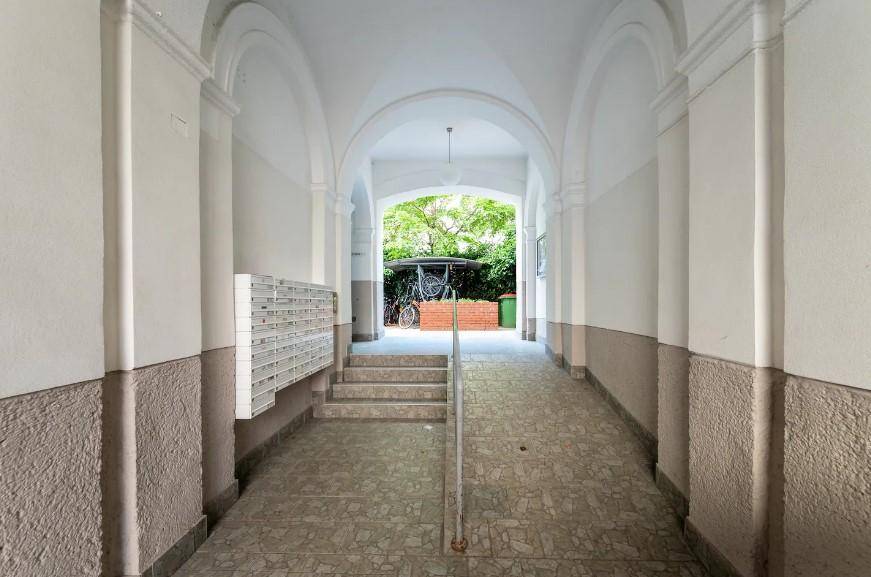 Historischer Eingangsbereich mit Briefkästen und Rampe, führt zu einem begrünten Innenhof.