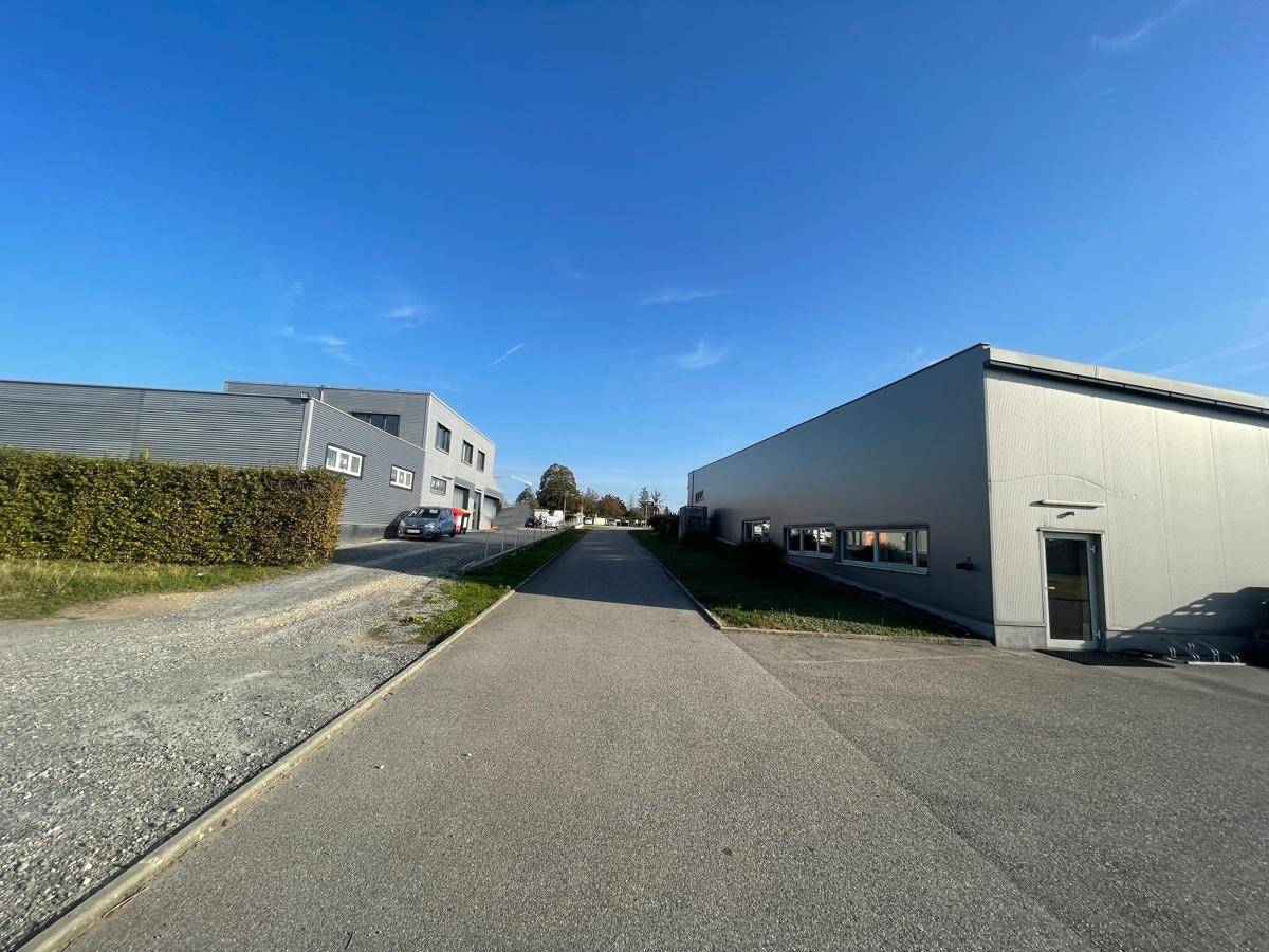 Zwei moderne Gewerbegebäude mit Zufahrtsstraße unter klarem blauem Himmel und gepflegter Hecke.