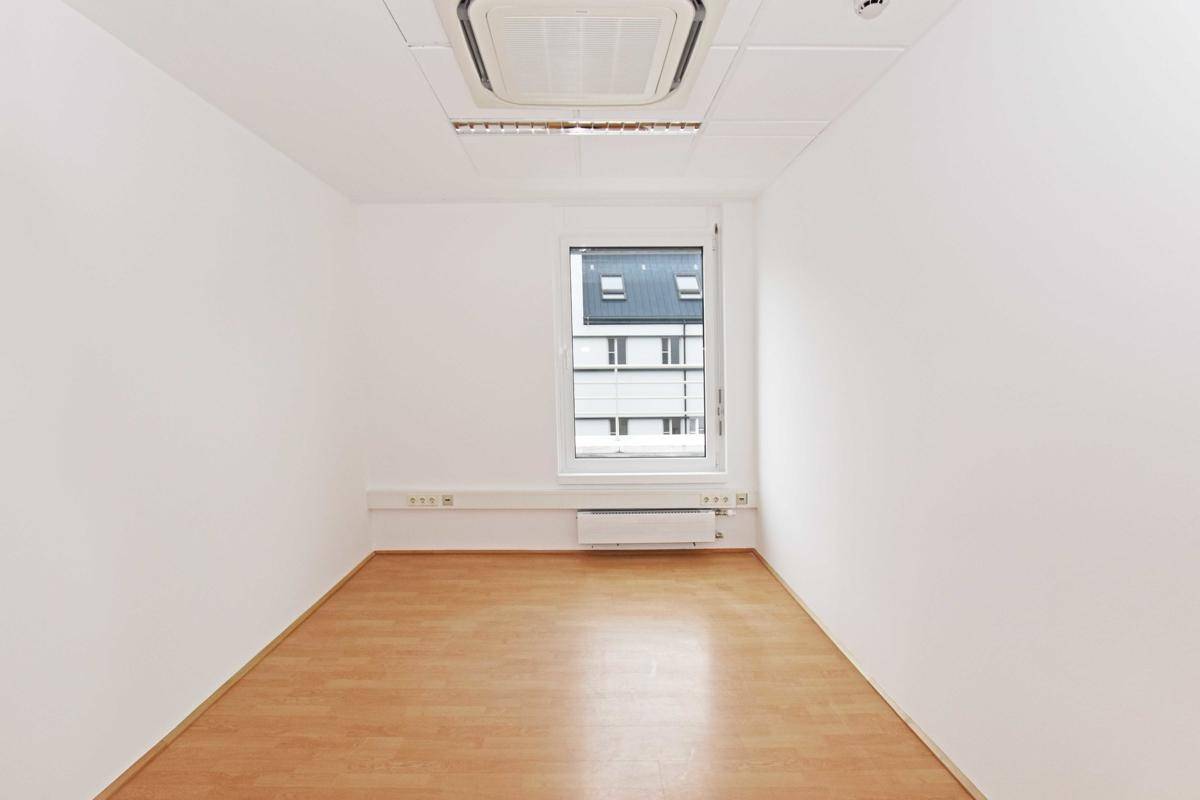 Kleines, helles Einzelbüro mit einem Fenster und Blick auf die umliegenden Gebäude, ausgestattet mit Klimaanlage.
