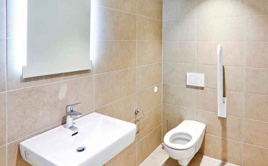 Barrierefreies Badezimmer mit wandhängender Toilette, Haltegriff und modernem Waschbecken für Komfort.