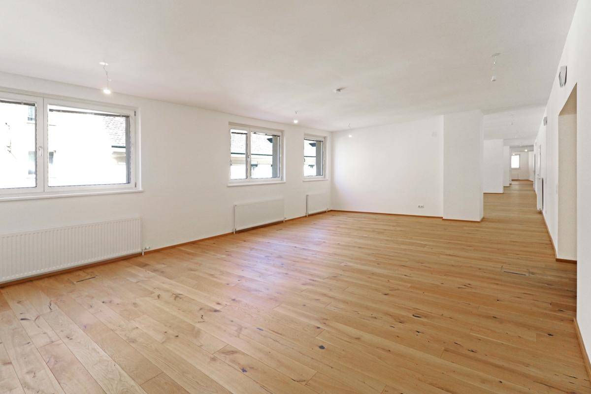 Geräumiger, heller Raum mit Holzboden und mehreren Fenstern, geeignet für Büros oder Verkaufsflächen.