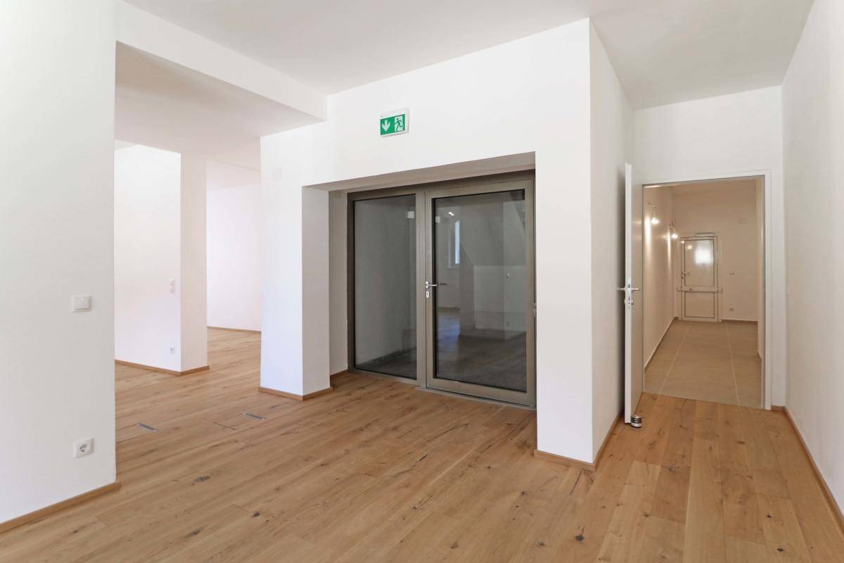 Heller Flur mit Holzboden und modernen Glastüren, der zu weiteren Räumen im Gebäude führt.