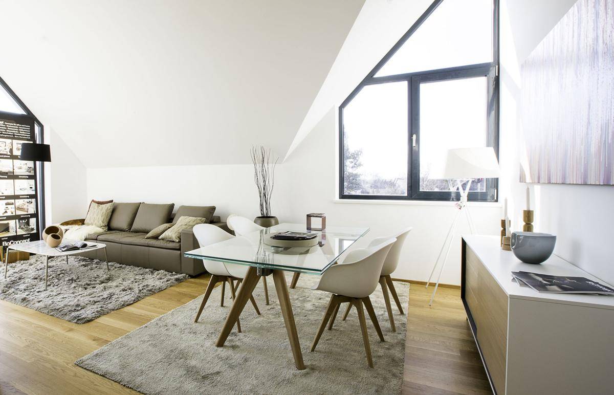 Gemütlicher Wohn-Essbereich mit Dachschrägen, Holzboden und einem großen Fenster, das den Raum erhellt.