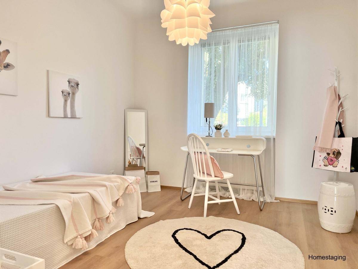 Freundliches Kinderzimmer mit hellem Laminatboden, Schreibtisch und verspielter Dekoration.