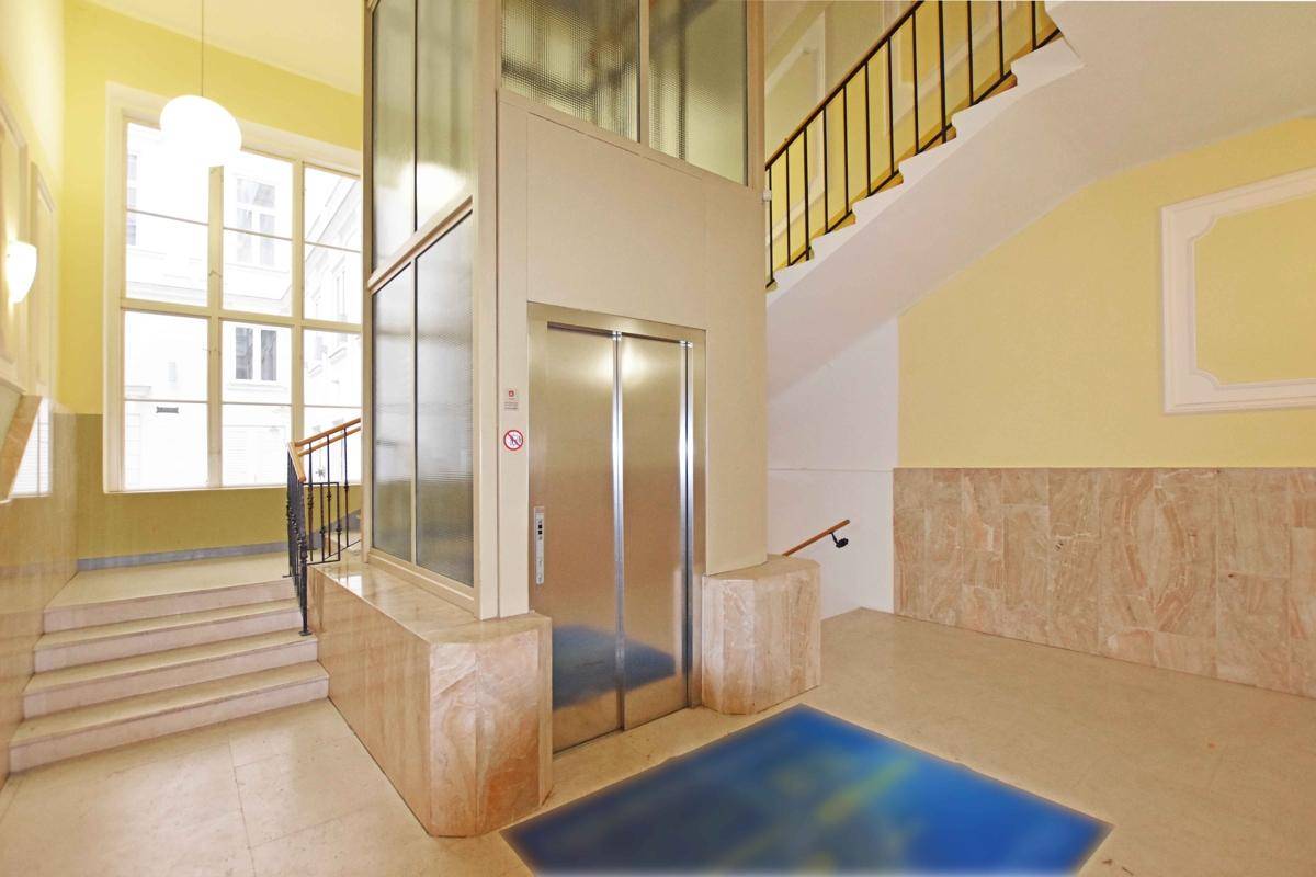 Heller Eingangsbereich mit modernem Glasaufzug, Marmorboden und einer eleganten Treppe.
