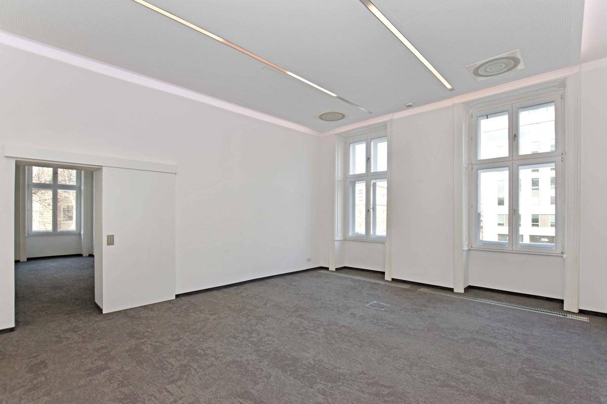 Geräumiger Büroraum mit modernem Teppichboden, großen Fenstern und integrierter Deckenbeleuchtung.