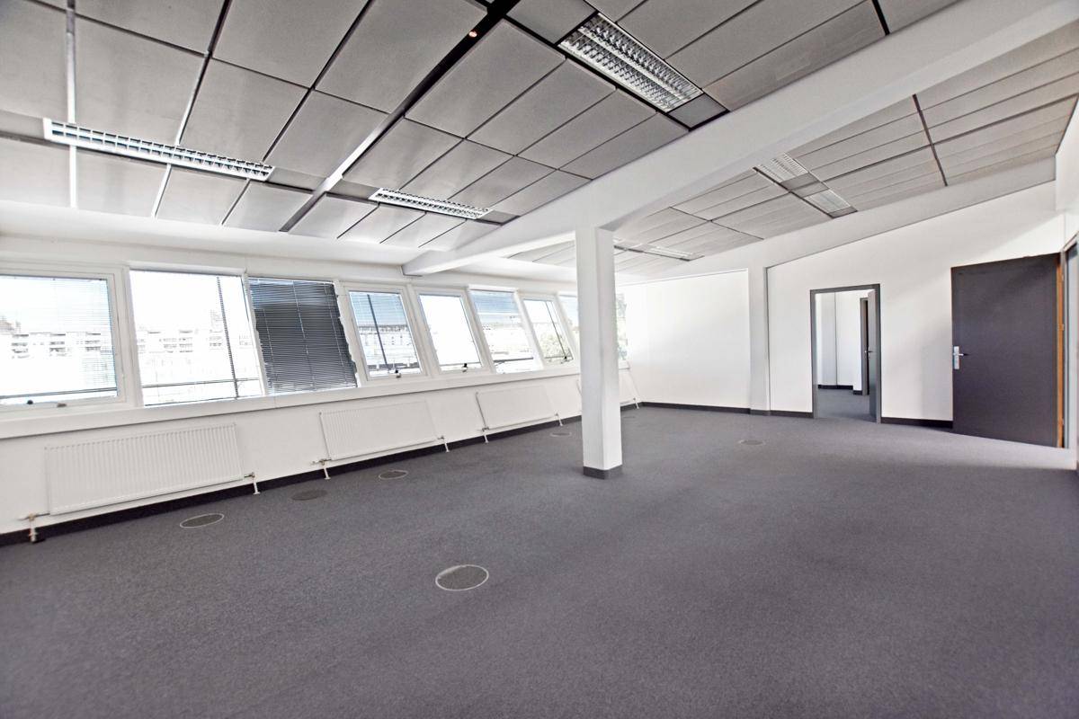 Geräumiger Bürobereich mit Teppichboden, vielen Fenstern und einer abgehängten Decke.