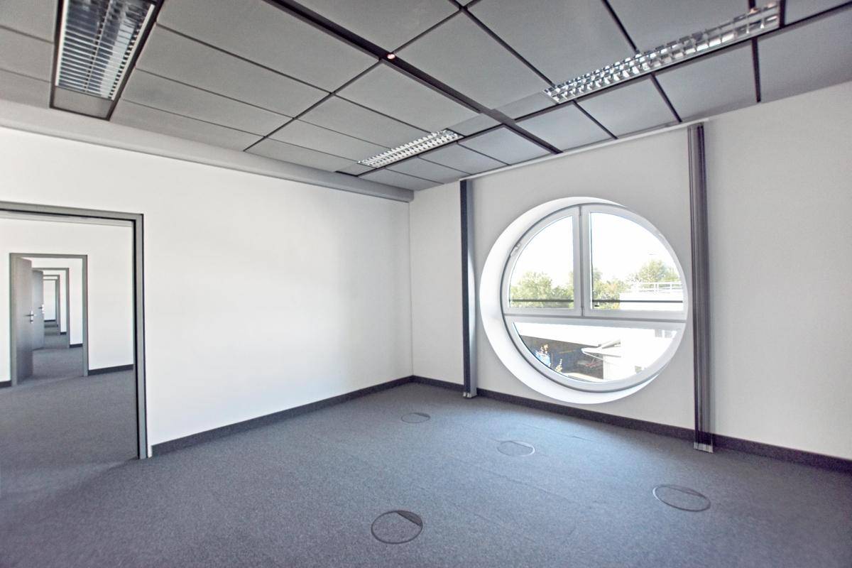 Moderner Büroraum mit Teppichboden, abgehängter Decke und einem einzigartigen runden Fenster.