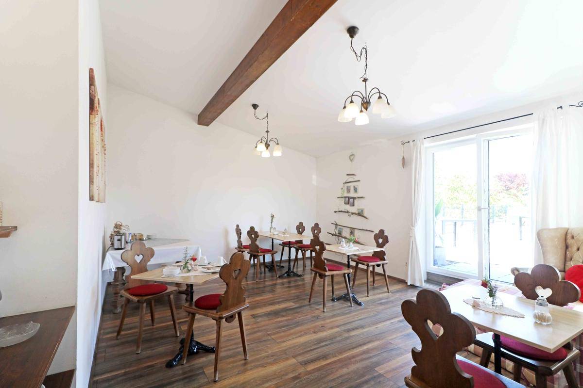 Heller Essbereich mit mehreren Holztischen und Stühlen im traditionellen Stil, Holzbalken an der Decke und Zugang zur Terrasse.