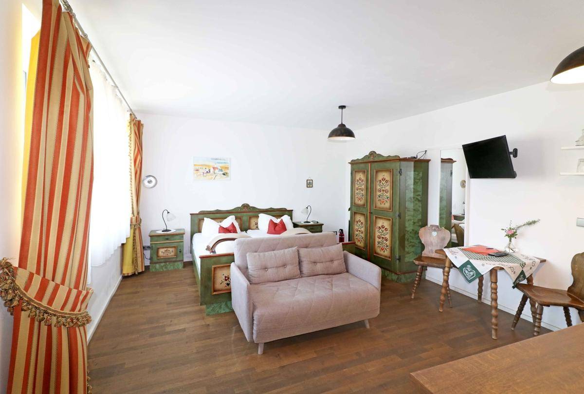 Gemütliches Schlafzimmer mit traditionellen, bemalten Holzmöbeln, einem Doppelbett und einem kleinen Sofa.